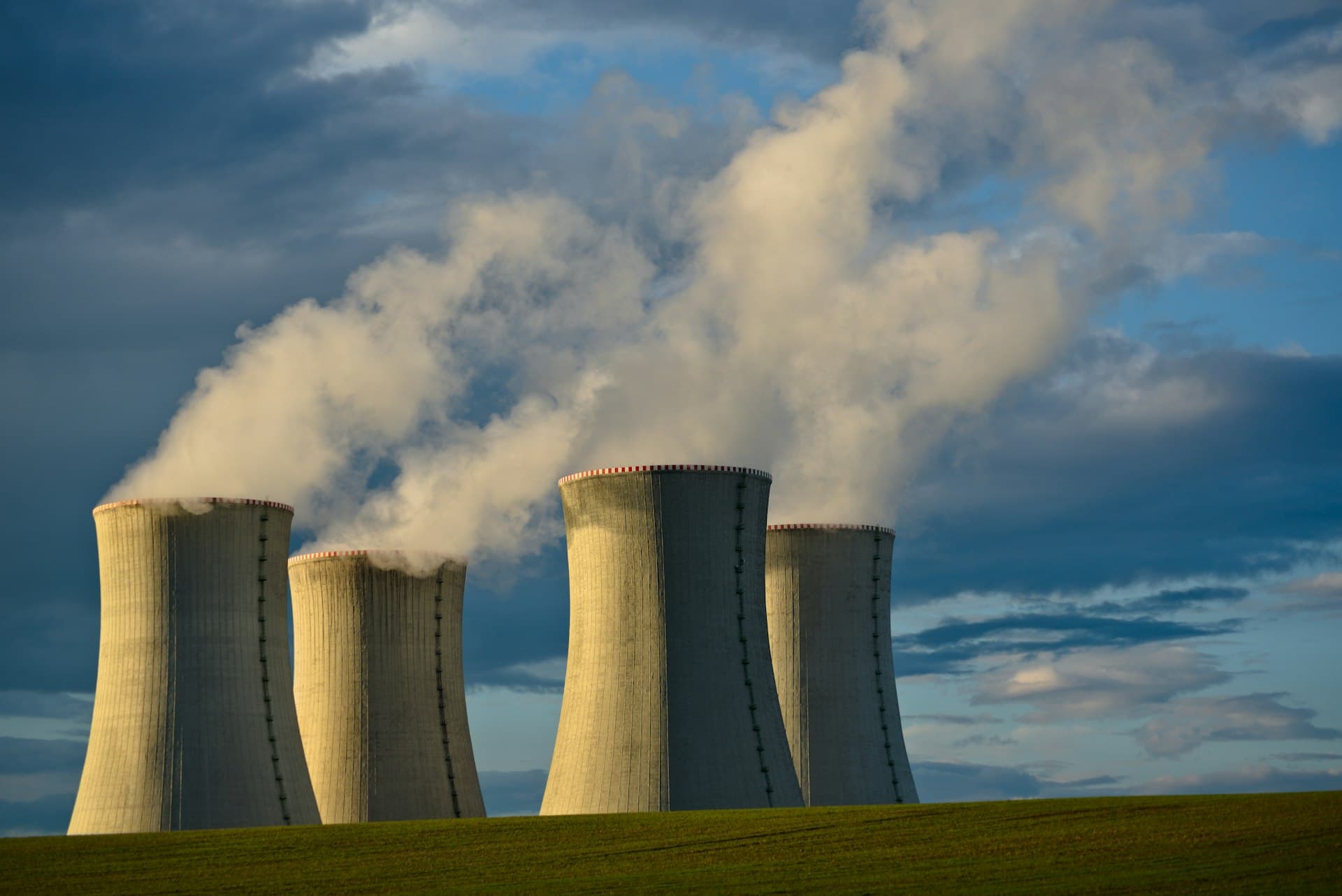 Nuclear power plant cooling towers releasing steam against a blue sky.